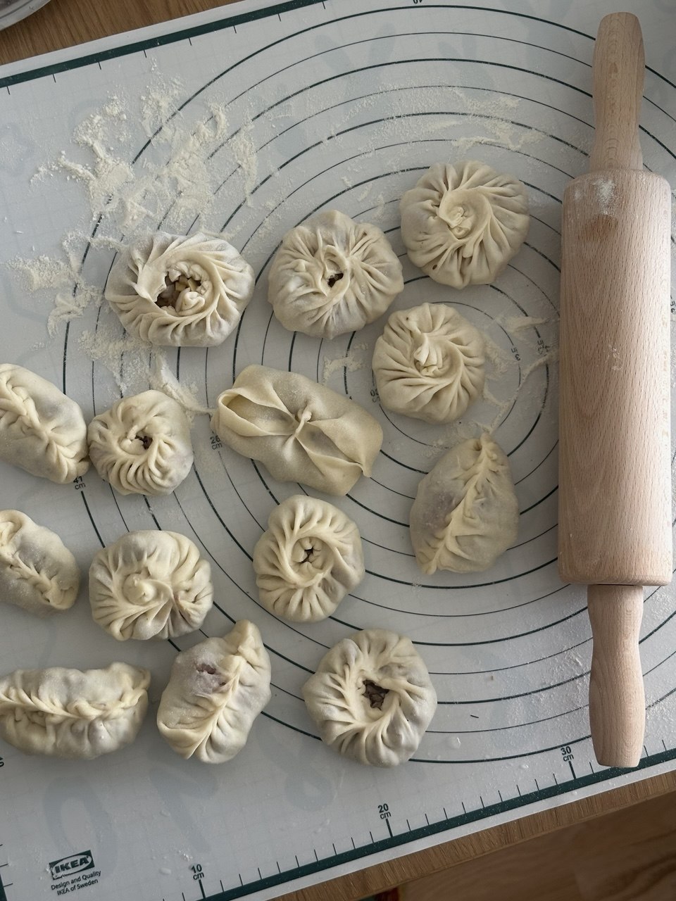 Handmade manty dumplings in different folded shapes next to a rolling pin